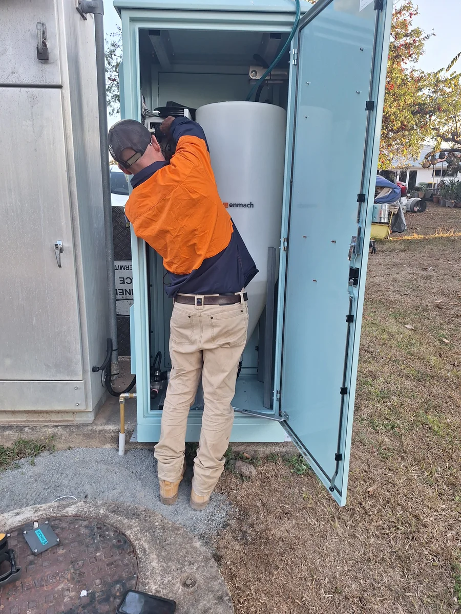 Field technician working at an open dosing cabinet beside a storage tank