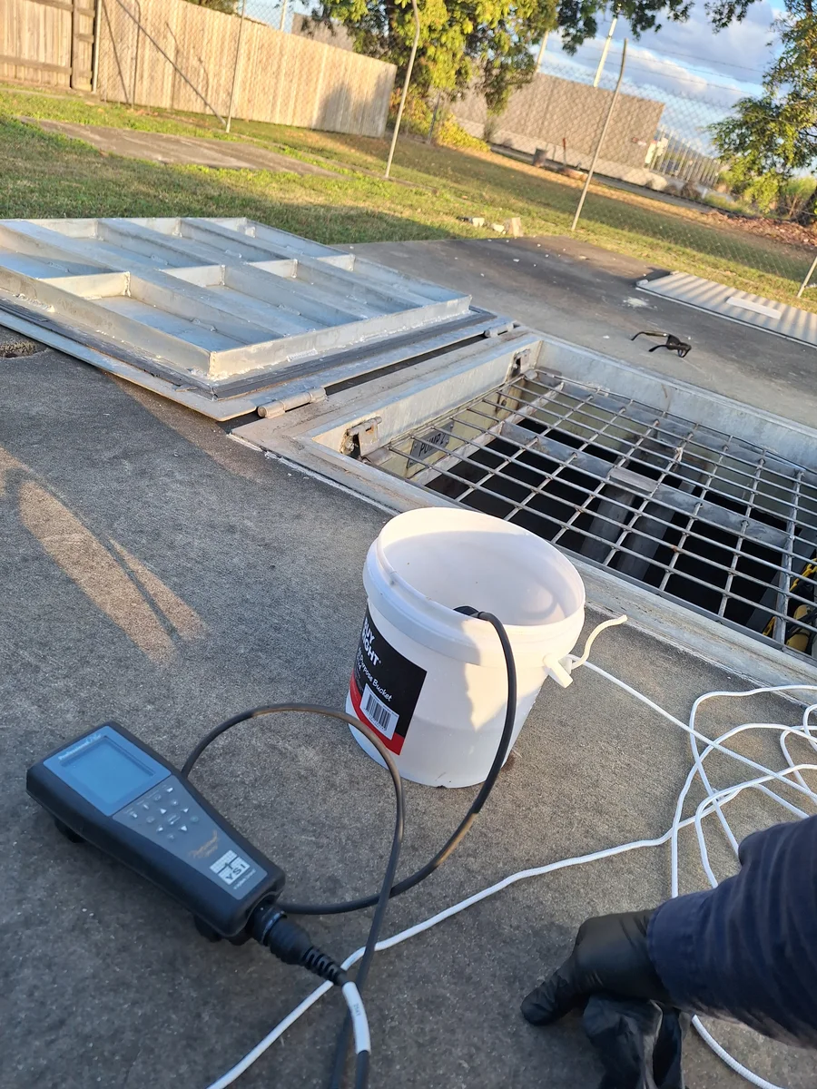 Water-quality meter, sampling bucket and probes beside an access opening